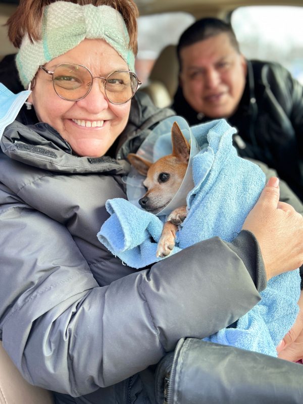 A woman holds a Chihuahua and smiles at the camera