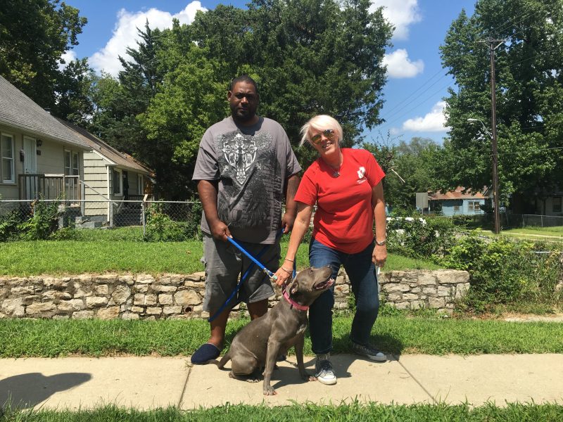 man and woman with dog on sidewalk