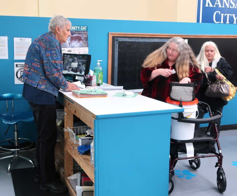 A woman stands behind a counter, talking with a woman on the other side.