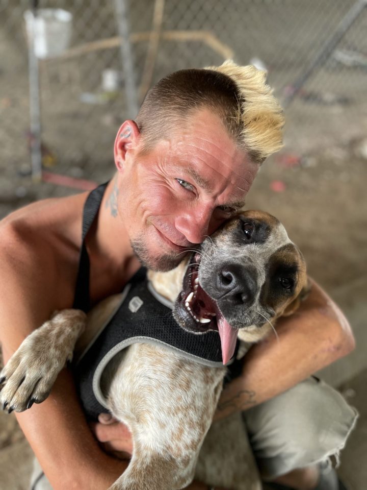 man and dog smiling while embracing one another