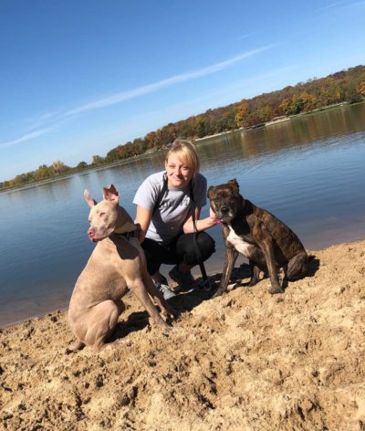 A woman stands on a lake shore with two dogs.