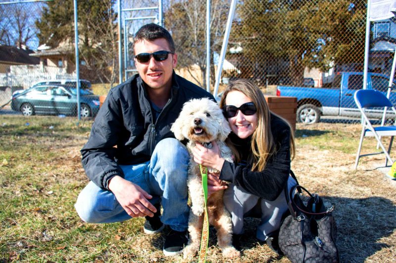 A man and a woman on either side of their fuzzy white dog