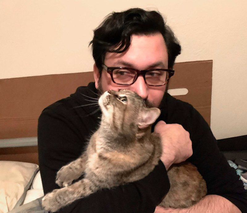  a man holds a cat and kisses her on the top of her head