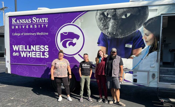 Four people stand next to the Kansas State mobile veterinary clinic