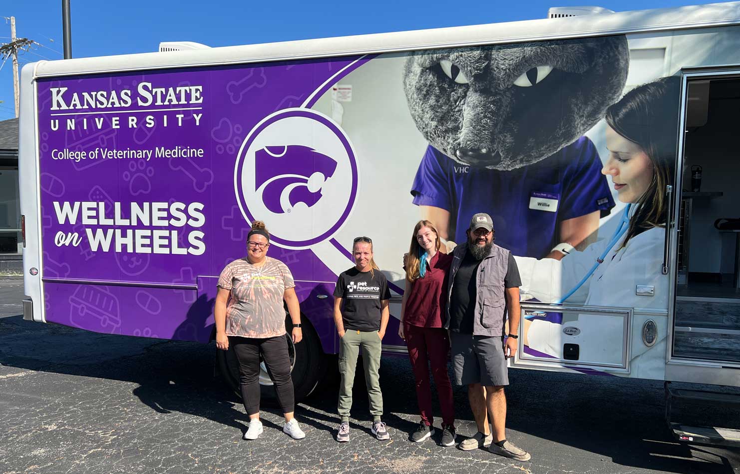 Four people stand next to the Kansas State mobile veterinary clinic