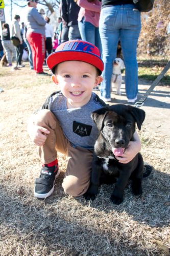 A young boy in a baseball cap crouches next to his pup and smiles