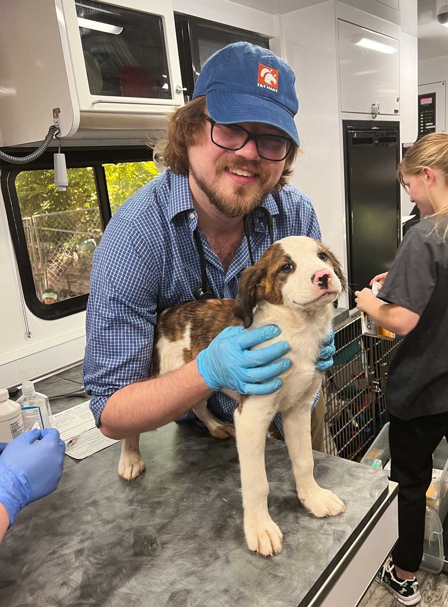 a vet student holds a puppy and looks at the camera