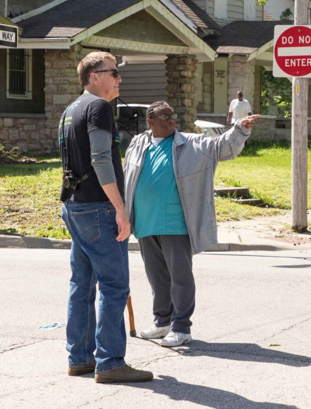 A man points off into the distance, indicating a house down the street.