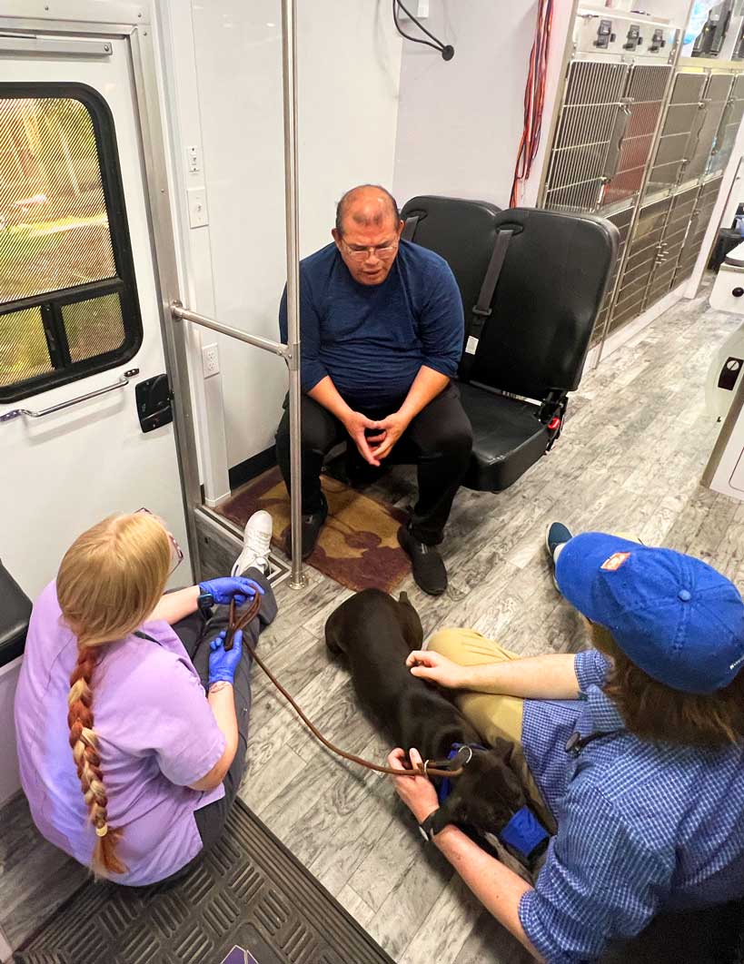 A client sits in a chair on the RV while the students sit with his dog, discussing options with him.